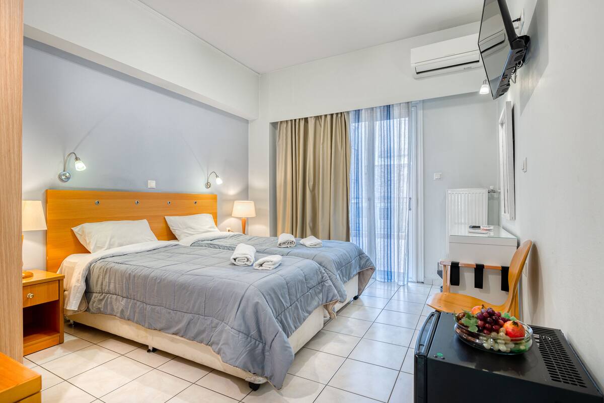 Quarto de hotel com duas camas, uma escrivaninha com uma cesta de frutas e uma televisão na parede.