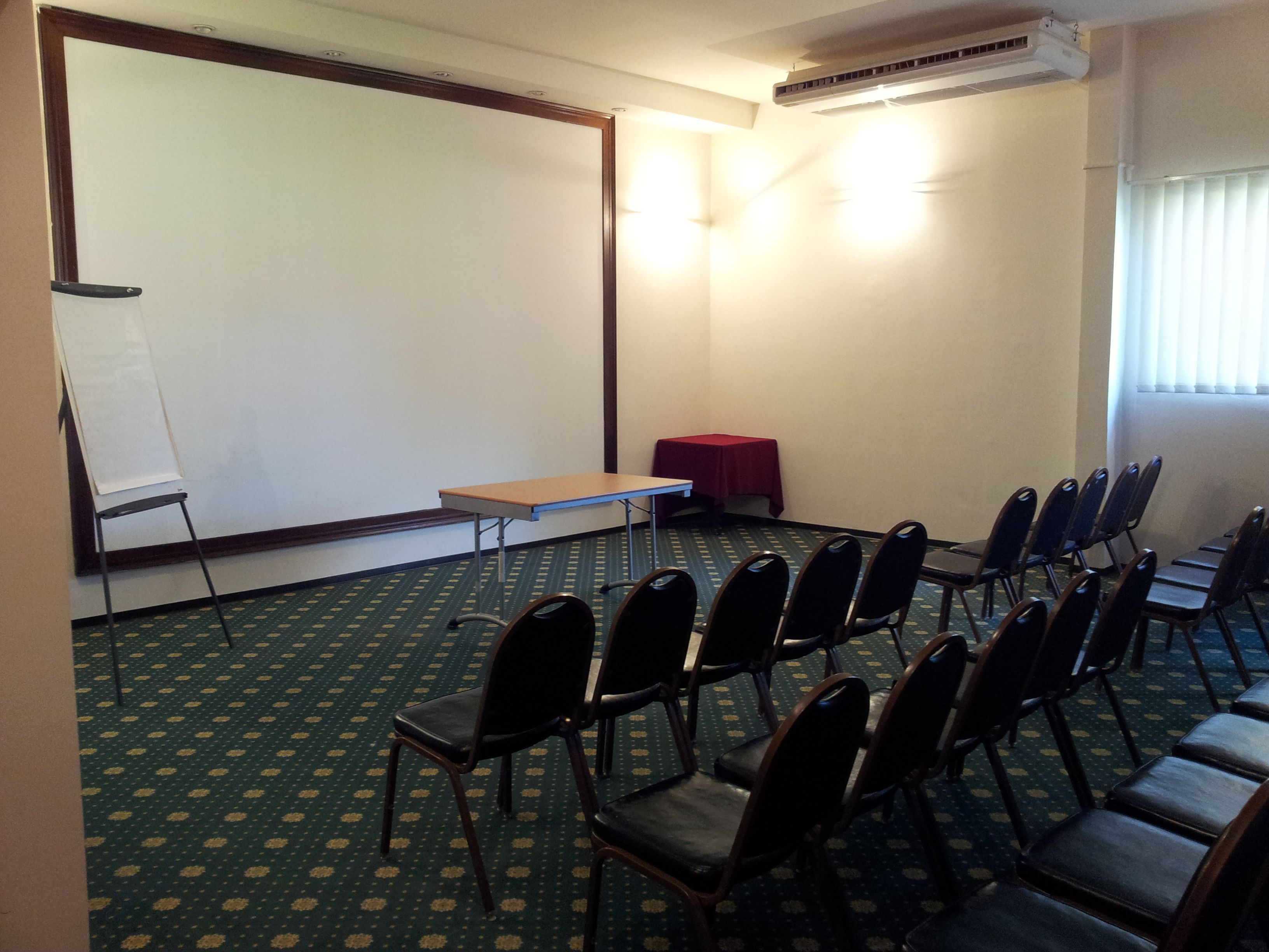 A conference room with a projector screen, a table, chairs, and an air conditioning unit.