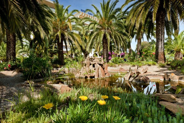 A hotel with a tropical garden, palm trees, and a pond.