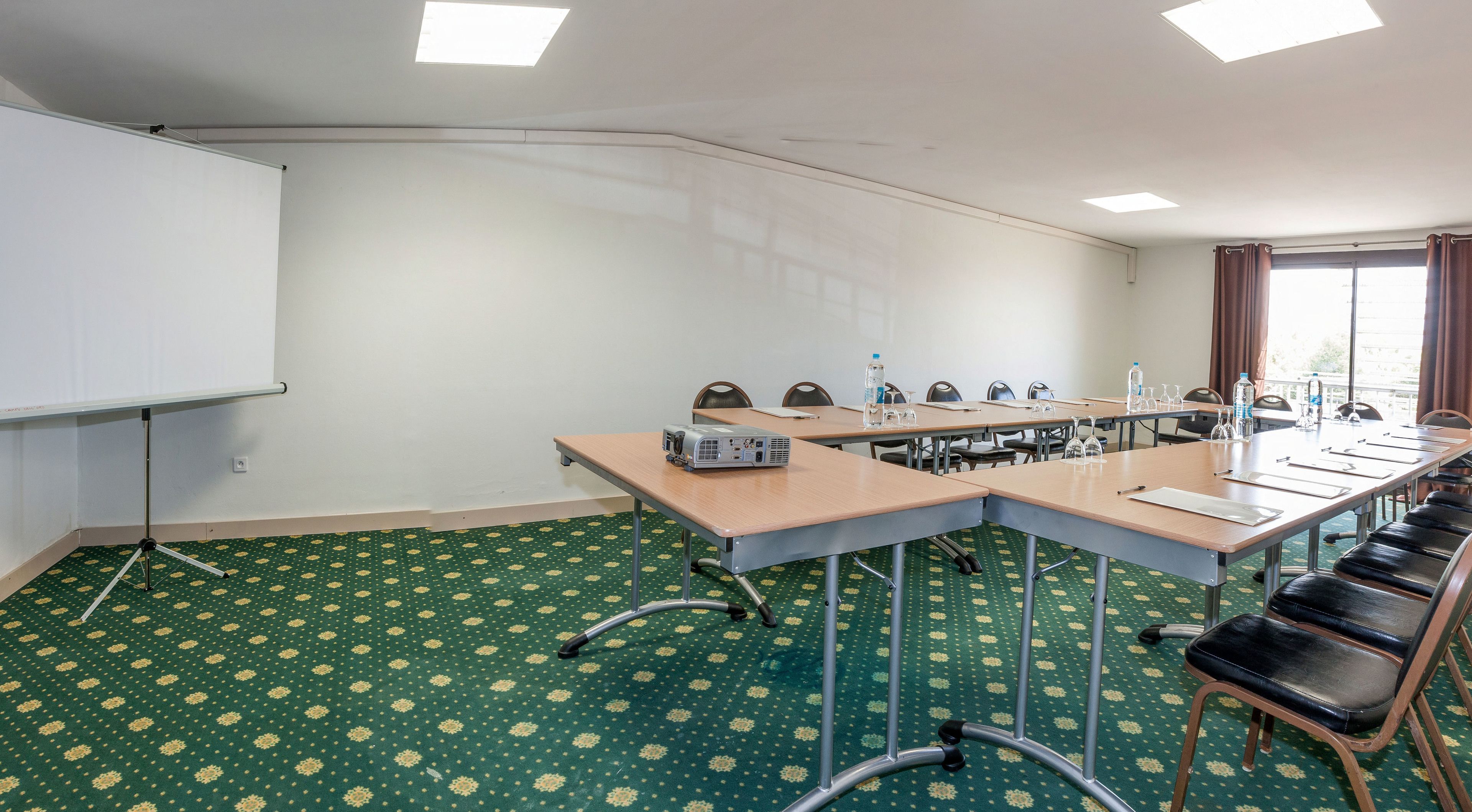 Un salón de conferencias con una larga mesa, sillas, un proyector y una pizarra.
