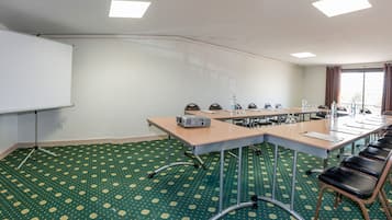Un salón de conferencias con una larga mesa, sillas, un proyector y una pizarra.
