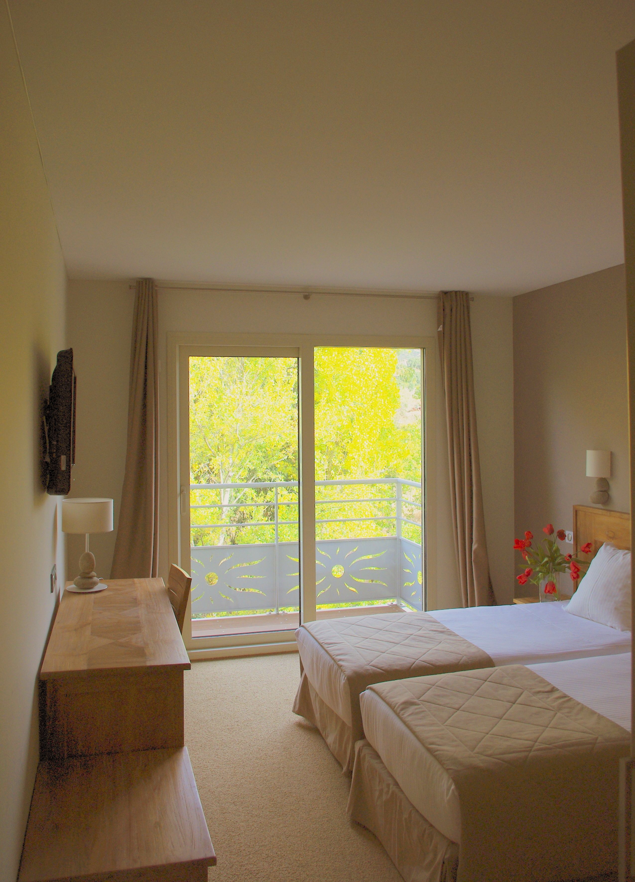Una habitación de hotel con cama, escritorio y vistas a la vegetación por la ventana.