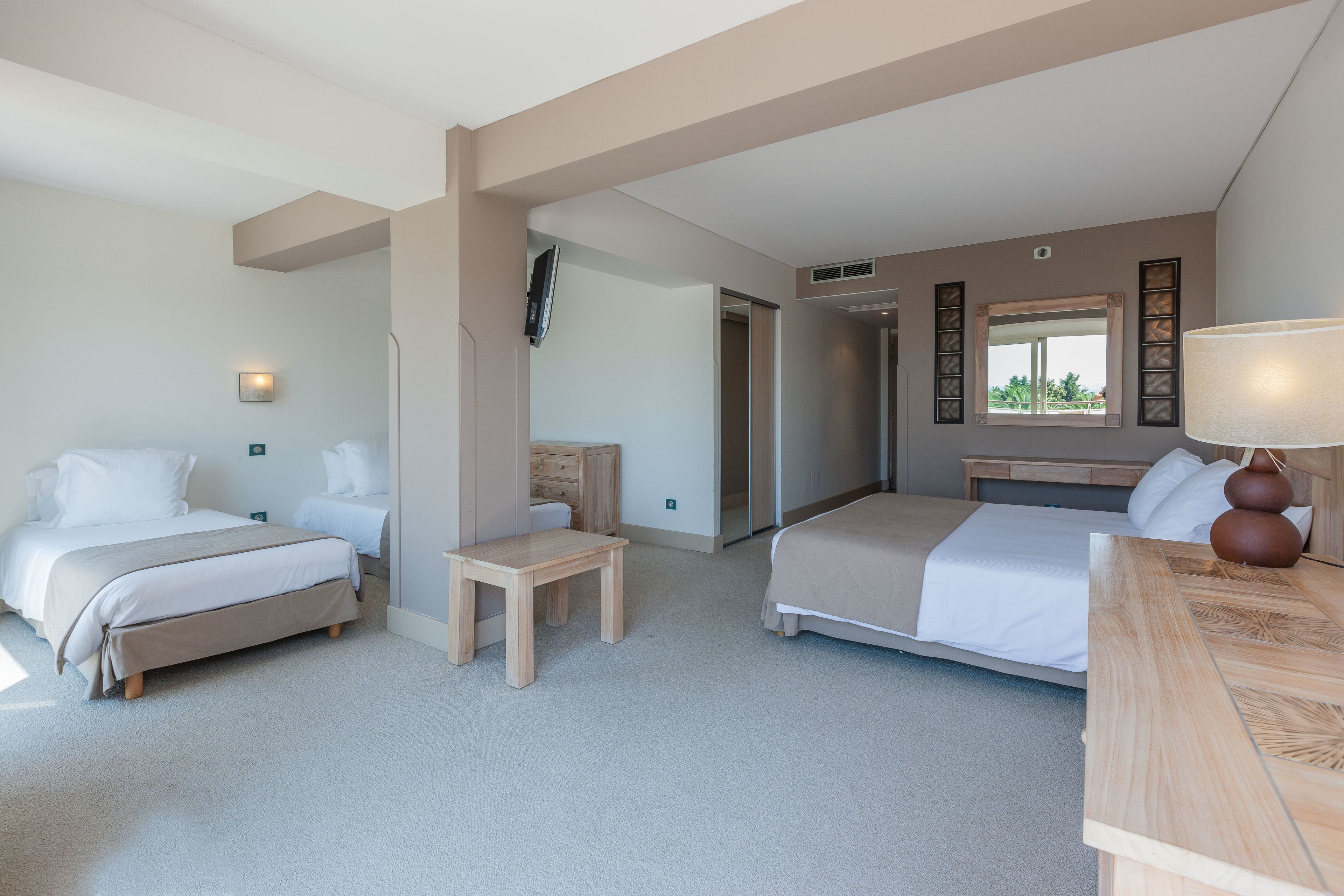 Een hotelkamer met twee bedden, een houten bureau, een spiegel en een raam met uitzicht.