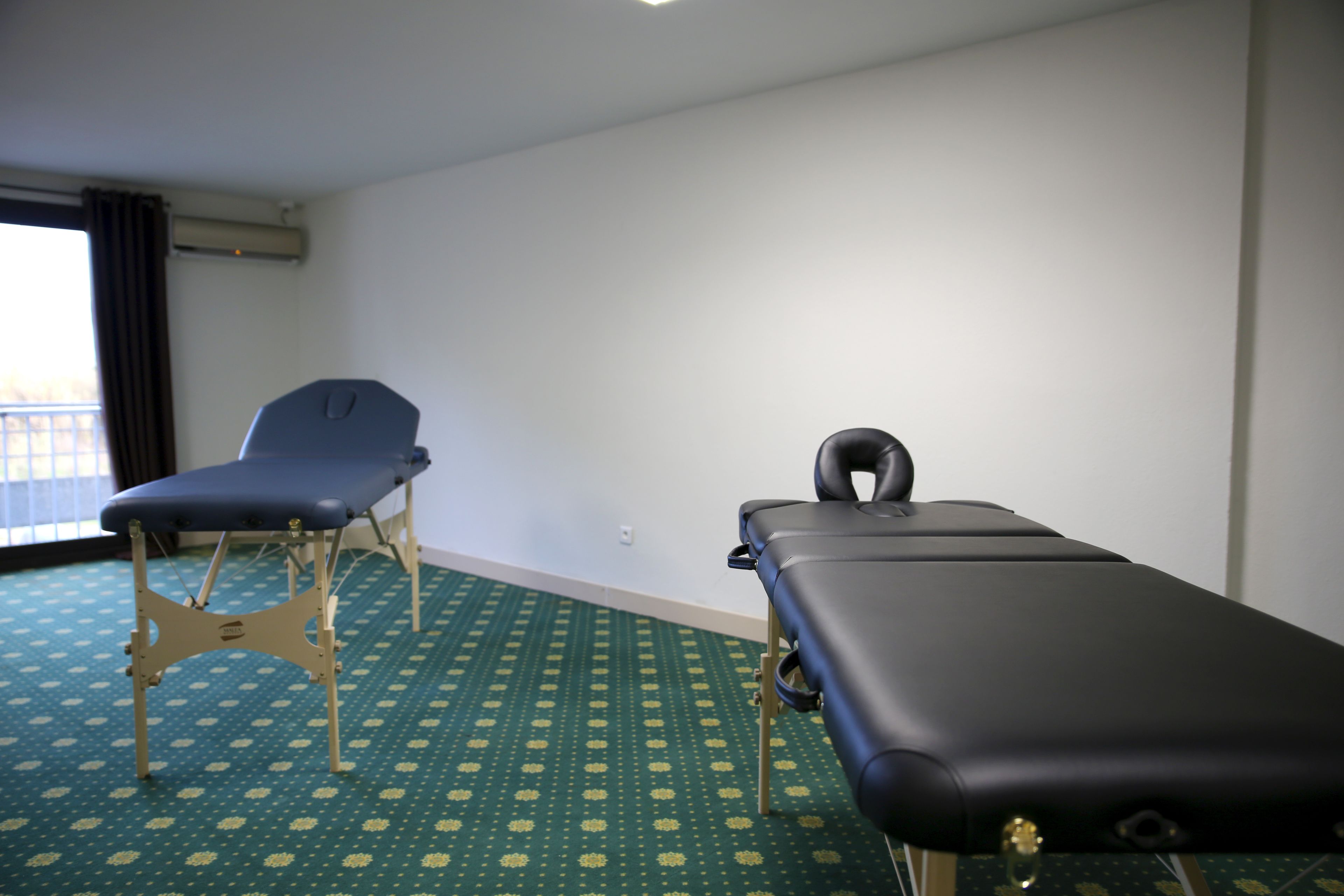 A room with a massage table, a massage chair, and a patterned carpet.