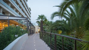 A pathway with a railing, surrounded by greenery and palm trees, leading to a building with multiple floors and large windows. - Campo Dell'Oro (Ajaccio)