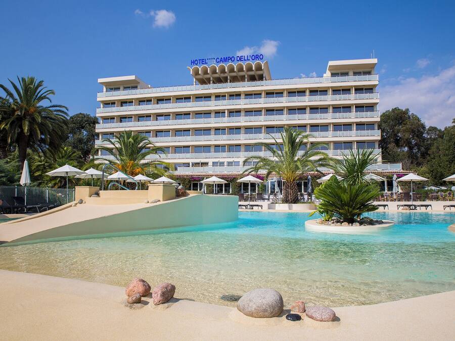 Un hotel con zona de piscina, palmeras y cielo azul despejado.