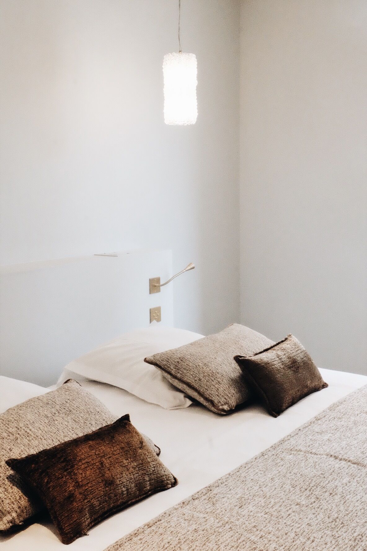 A bedroom with a bed, pillows, a hanging light fixture, and a wall-mounted switch.