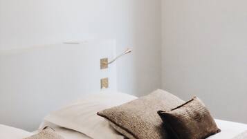 Une chambre à coucher avec un lit, des oreillers, un luminaire suspendu et un interrupteur fixé au mur.