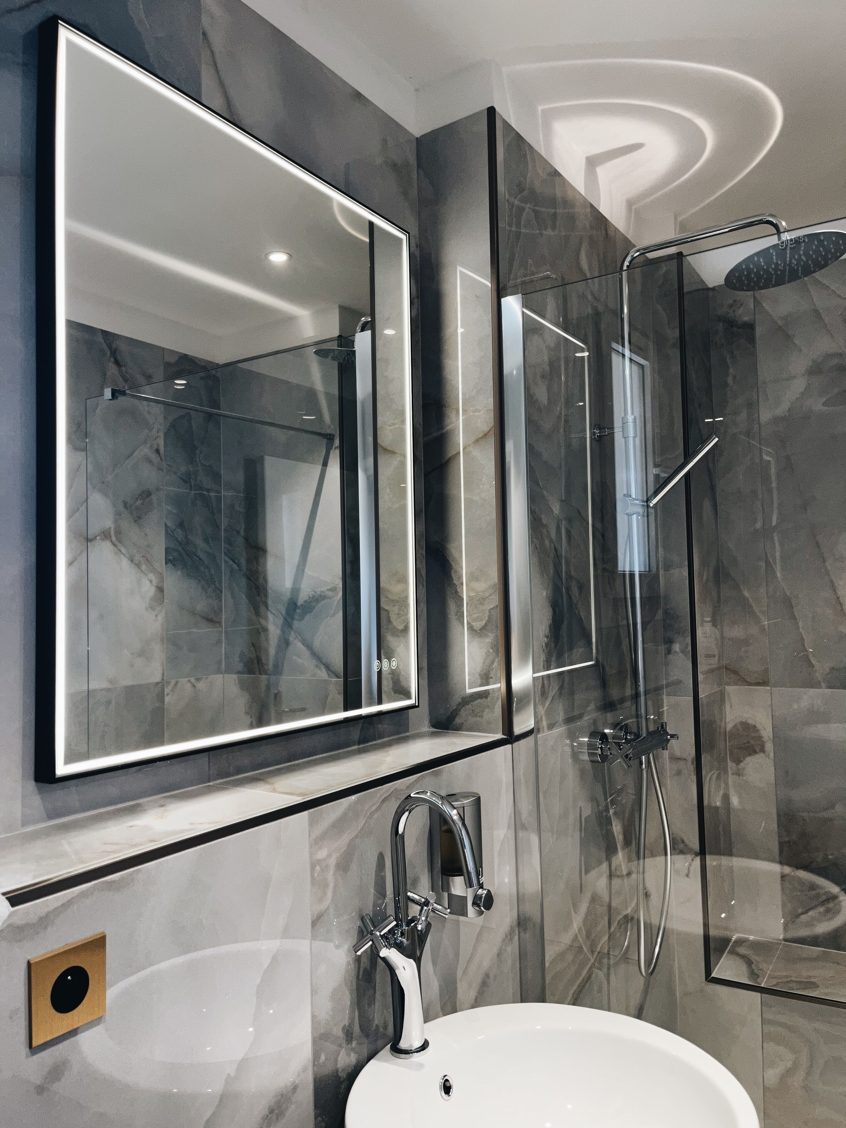 A modern bathroom with a large mirror, a sink, and a glass-enclosed shower.