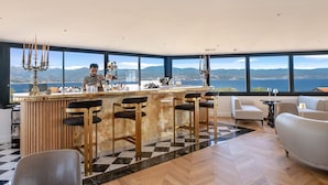 A modern bar area with a view of the sea and mountains, bar stools, and a seating area with a checkered floor. - Hotel San Carlu Citadelle (Ajaccio)