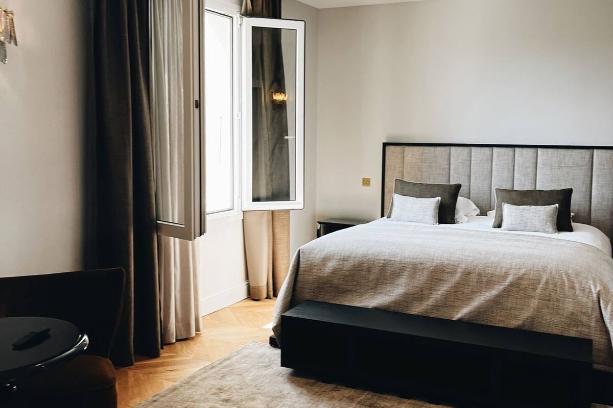 A modern bedroom with a large bed, a desk, and a window with curtains.
