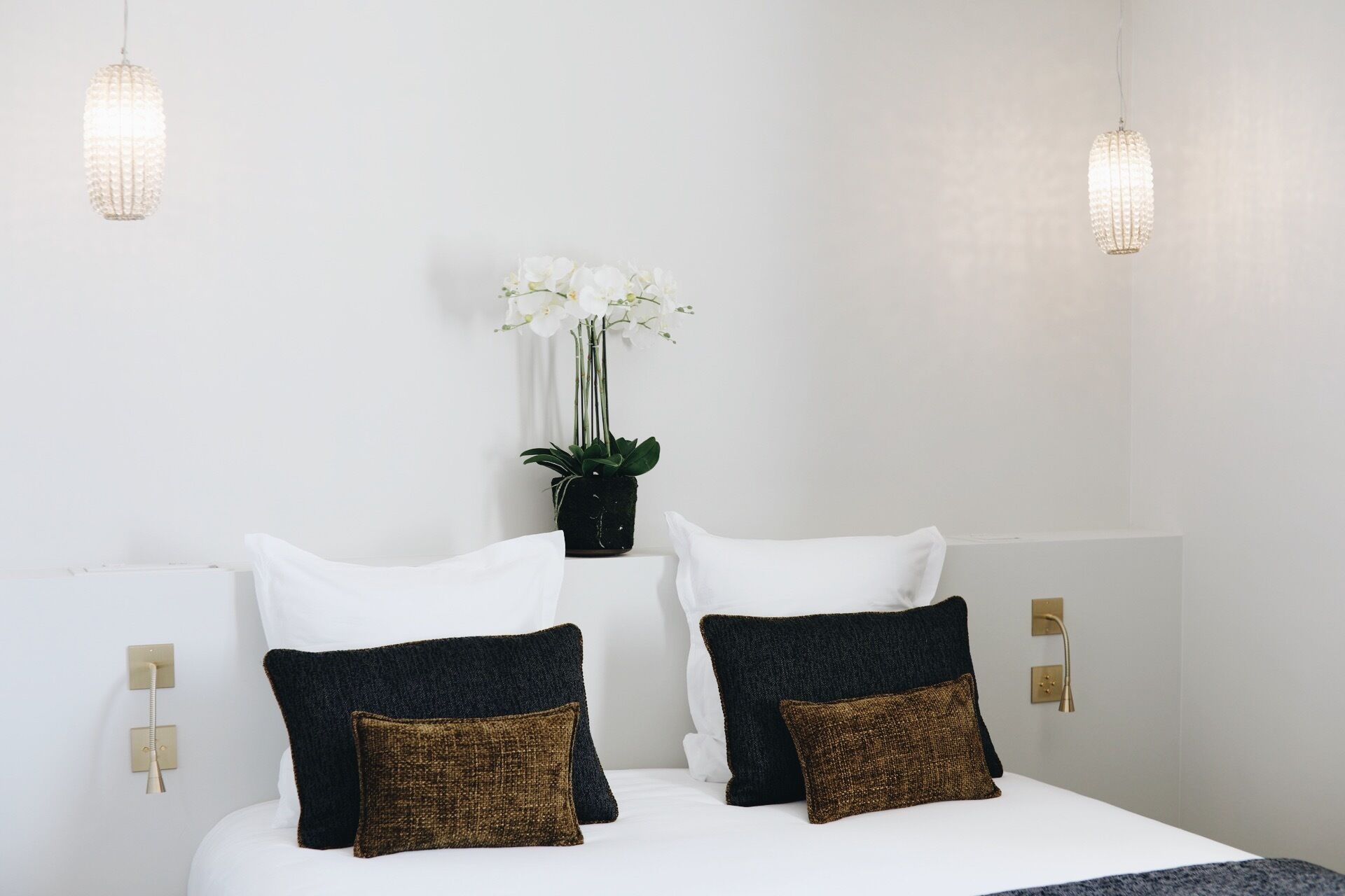 Une chambre à coucher avec un lit, des oreillers blancs, une plante en pot et deux lampes fixées au mur.