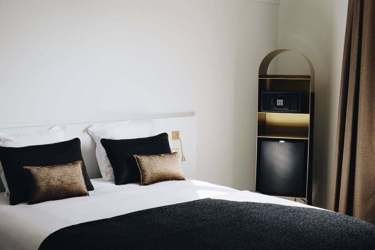 Una habitación de hotel con una cama, dos almohadas, una mesita de noche, un armario y un espejo.