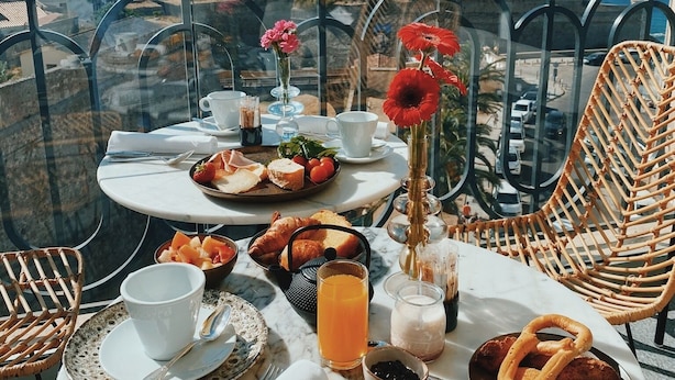 A balcony table with breakfast items, a wicker chair, and a scenic view of the sea and mountains. - Hotel San Carlu Citadelle (Ajaccio)