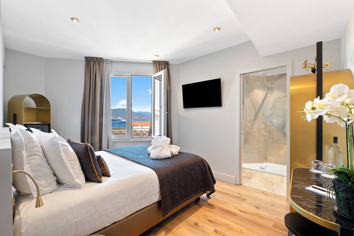 Una habitación de hotel moderna con una cama grande, televisión, ducha y vistas al exterior.