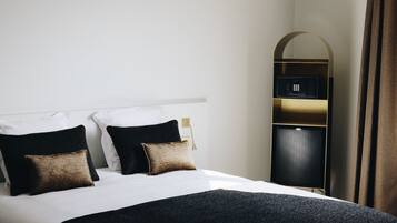 A hotel room with a bed, two pillows, a bedside table, a mirror, a wardrobe, and a curtain.
