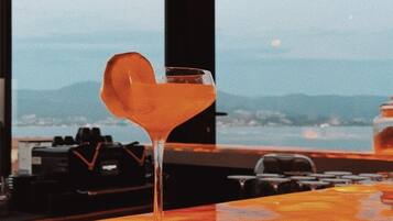 A bar with a martini glass on the counter, a view of mountains, and a sunset in the background.