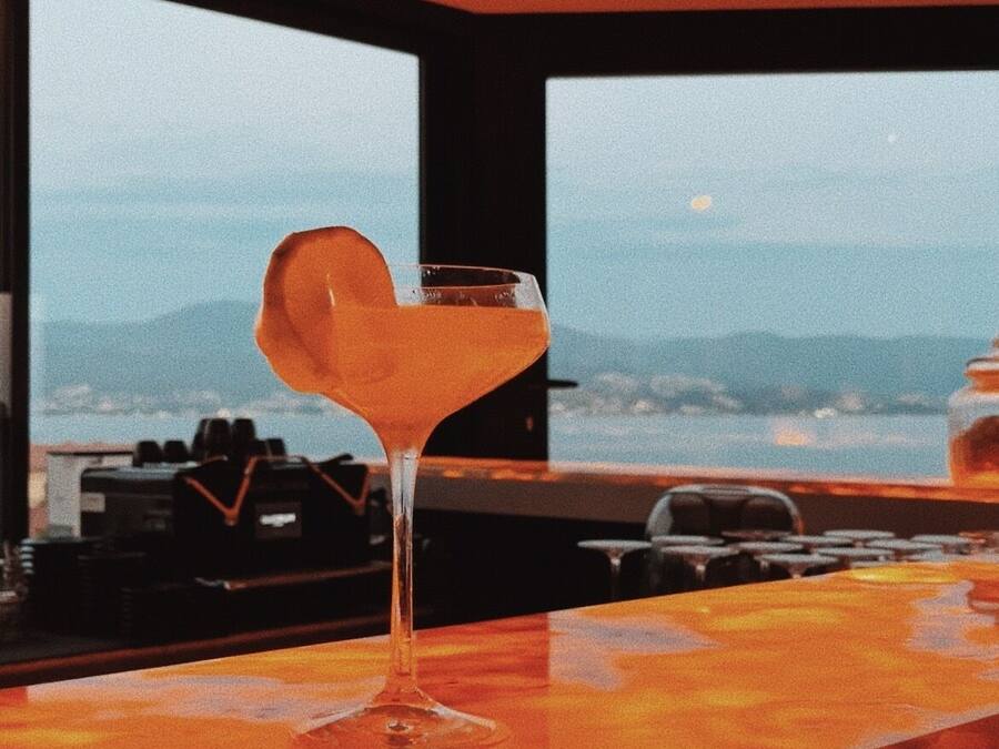 A bar with a martini glass on the counter, a view of mountains, and a sunset in the background.