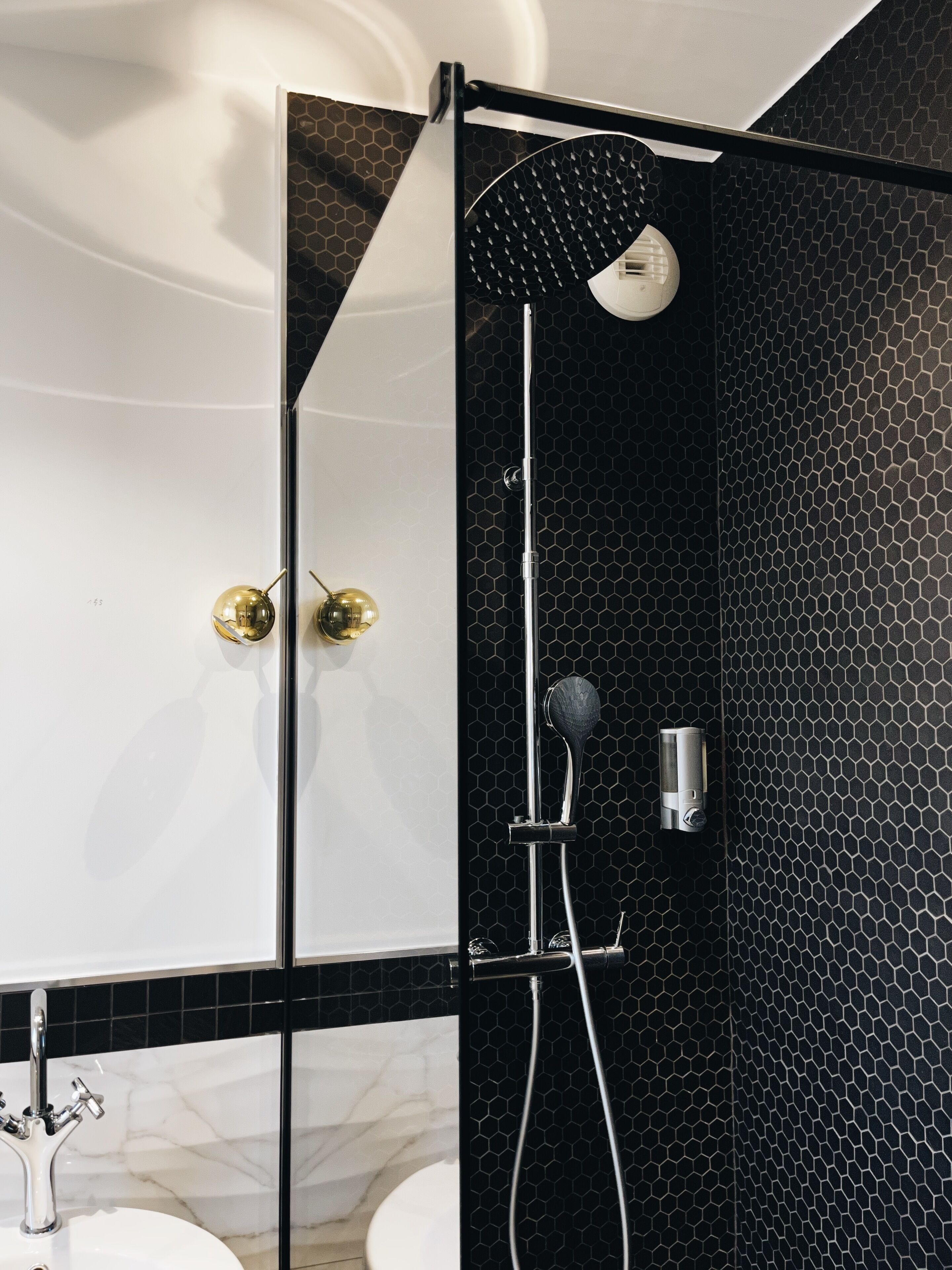 Een moderne badkamer met een douchewand betegeld met zwarte honingraat tegels, een wit bad en een marmeren wastafel.