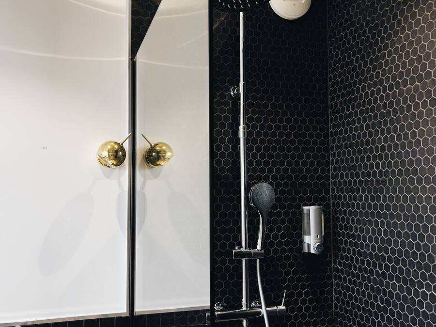 Een moderne badkamer met een douchewand betegeld met zwarte honingraat tegels, een wit bad en een marmeren wastafel.