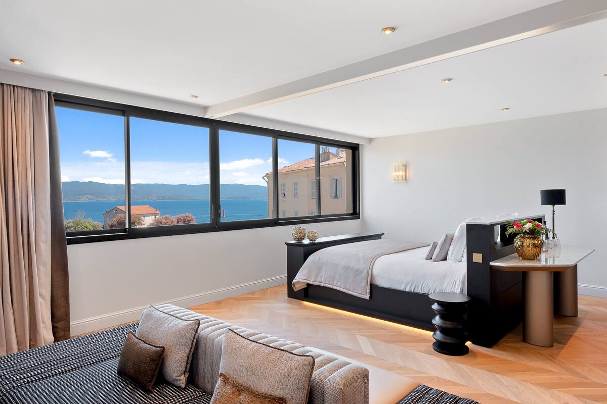 Un dormitorio moderno con un ventanal grande, una cama, una mesita de noche y un sofá.
