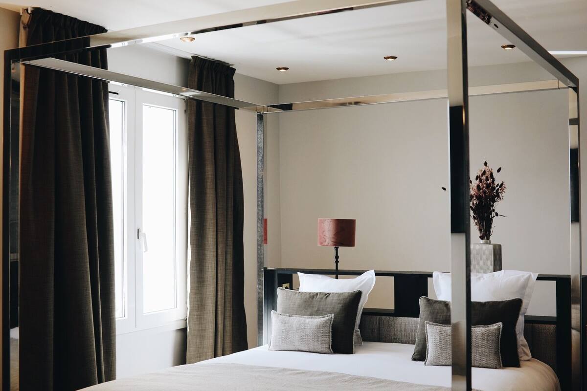 Un dormitorio moderno con una cama con dosel, una lámpara de noche y un florero con flores secas sobre la mesita de noche.