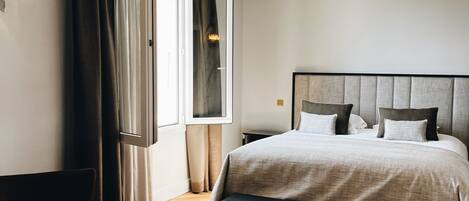 A modern bedroom with a large bed, a desk, and a window with curtains.