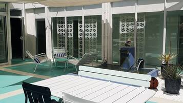 A rooftop pool area with a table and chairs, surrounded by glass doors with decorative screens, and a view of a modern building in the background.
