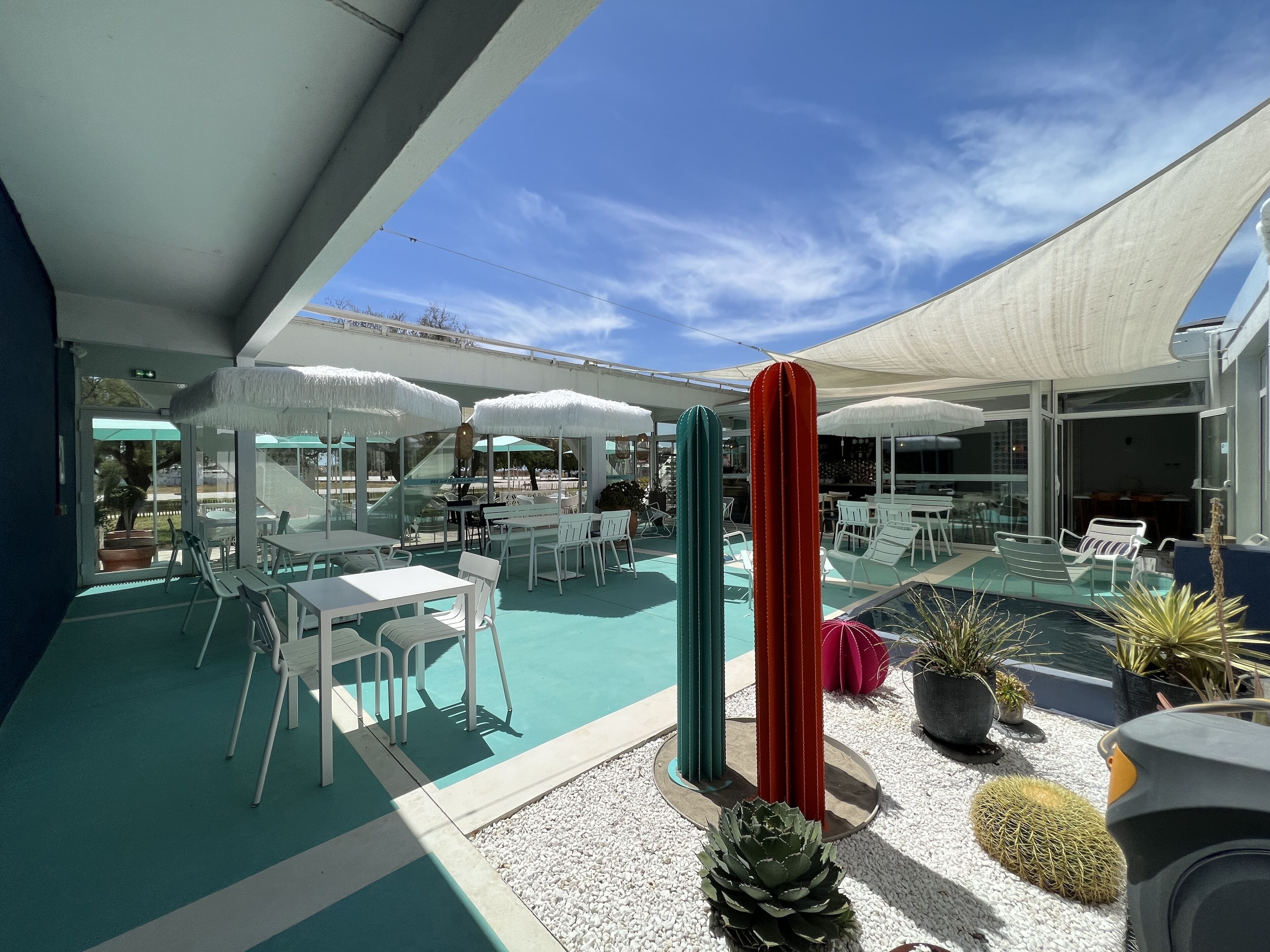 Ein Terrassenbereich im Freien mit weißen Tischen und Stühlen, einem Pool und verschiedenen Pflanzen.
