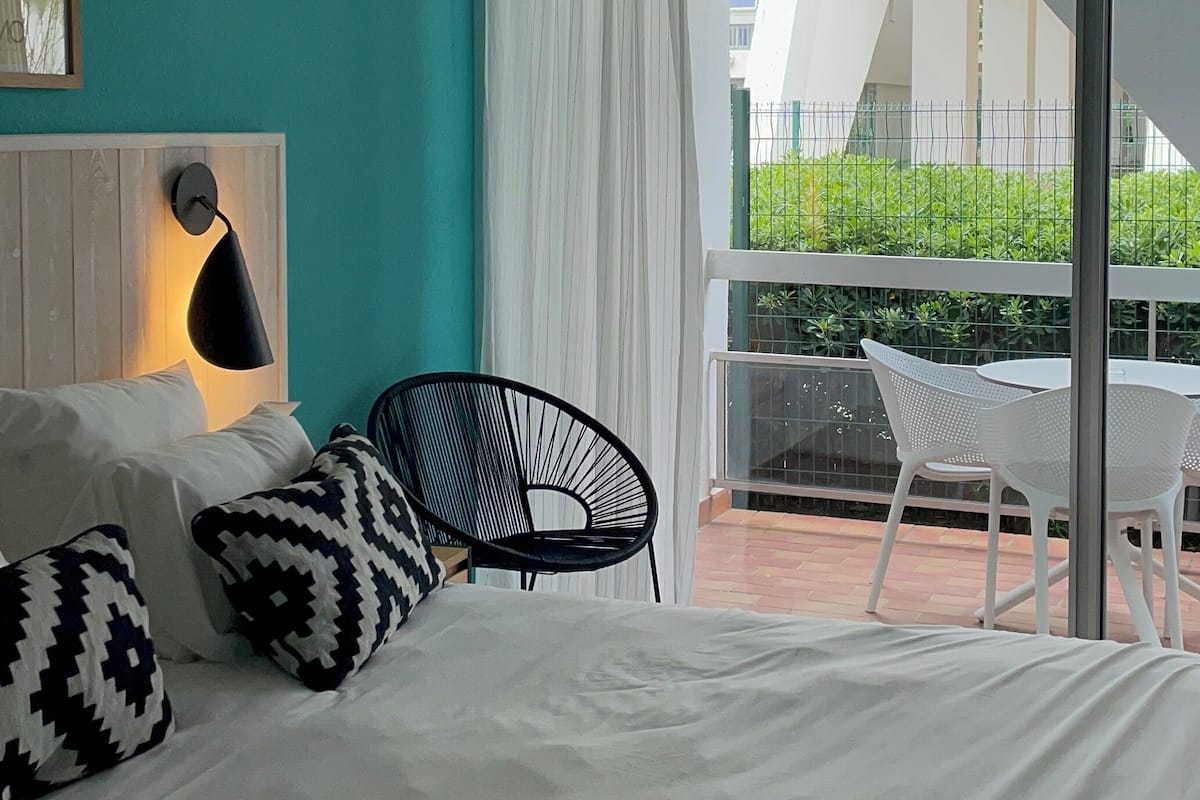 A bedroom with a bed, a chair, and a view of the outside balcony.