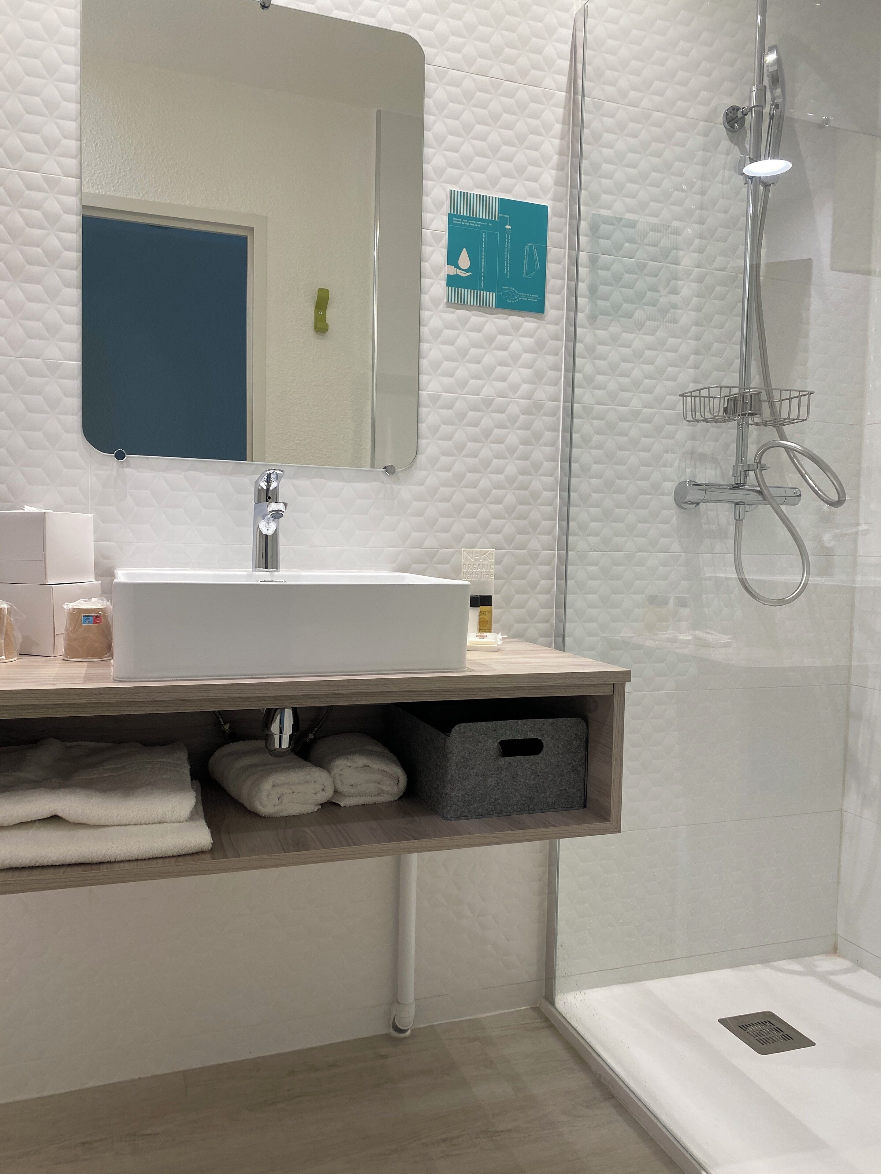 A modern bathroom with a white sink, mirror, and shower. There are towels and toiletries on the counter.