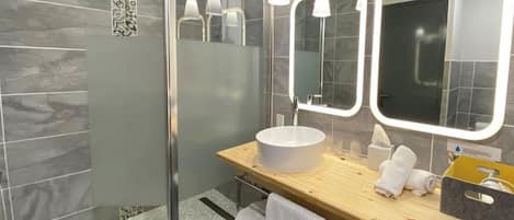 Un baño moderno con un espejo grande, un lavabo redondo y una zona de ducha.