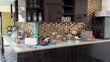 Eine moderne Küche mit Bar, ein geometrisches Rückwandmuster, eine Arbeitsplatte mit verschiedenen Küchengeräten und ein Essbereich mit weißem Tisch und Stühlen.