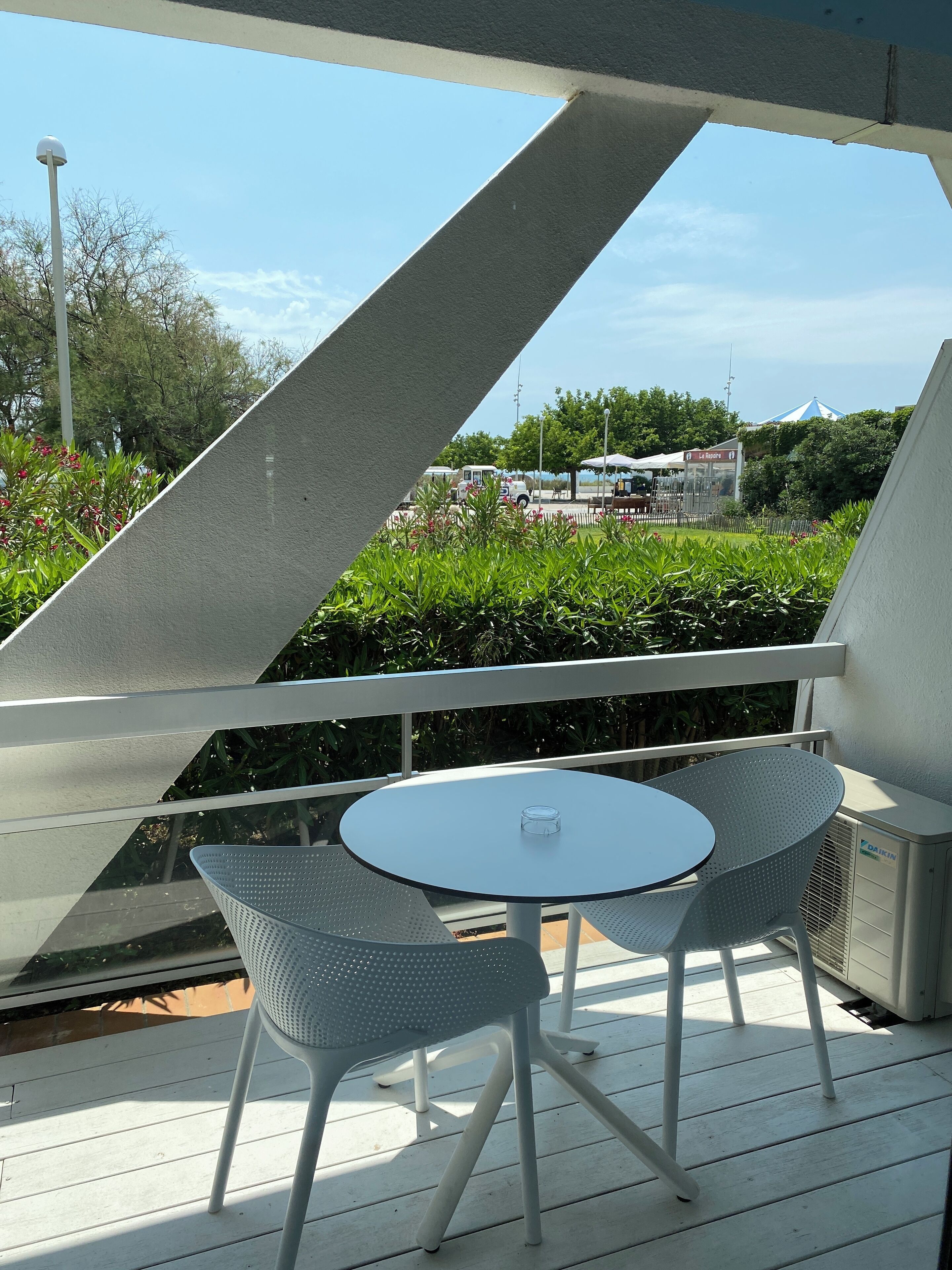 Un espacio de estar al aire libre con techo, con una mesa redonda y dos sillas, con vistas a un jardín y un edificio con un letrero que dice "La Roca's".
