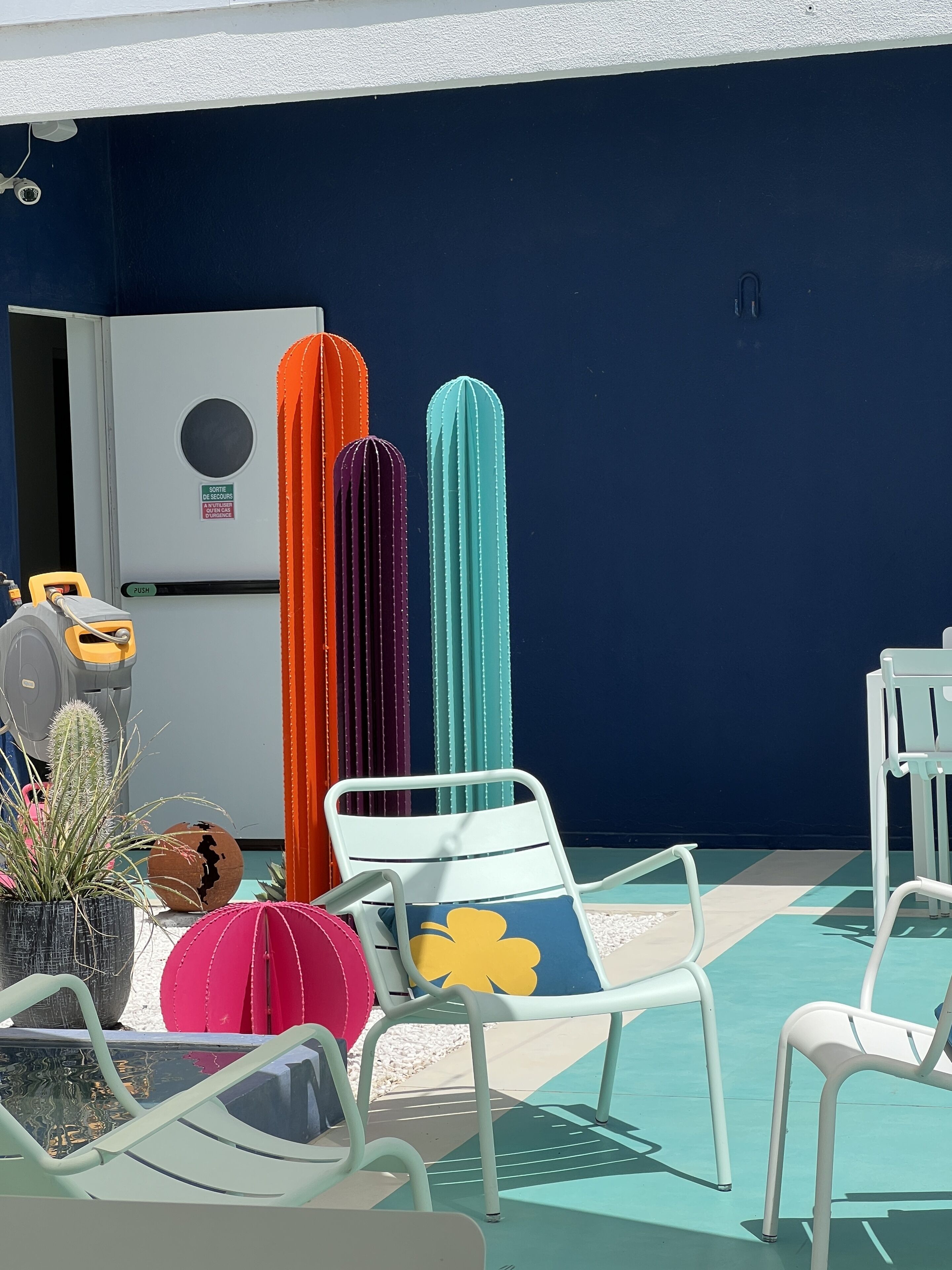 Een terras met buitenmeubilair, een afvalbak en een beveiligingscamera aan de muur.