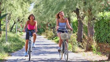 Dos personas andando en bicicleta por un camino pavimentado rodeado de árboles y follaje.