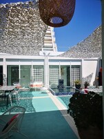 Un área de piscina moderna al aire libre con sillones de descanso, una piscina pequeña y una cerca blanca decorativa.