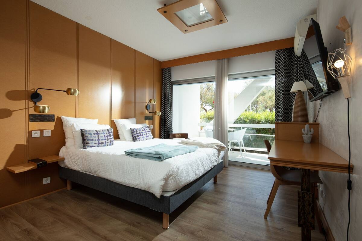 A modern bedroom with a large bed, bedside tables, a desk, and a view of the outdoors.