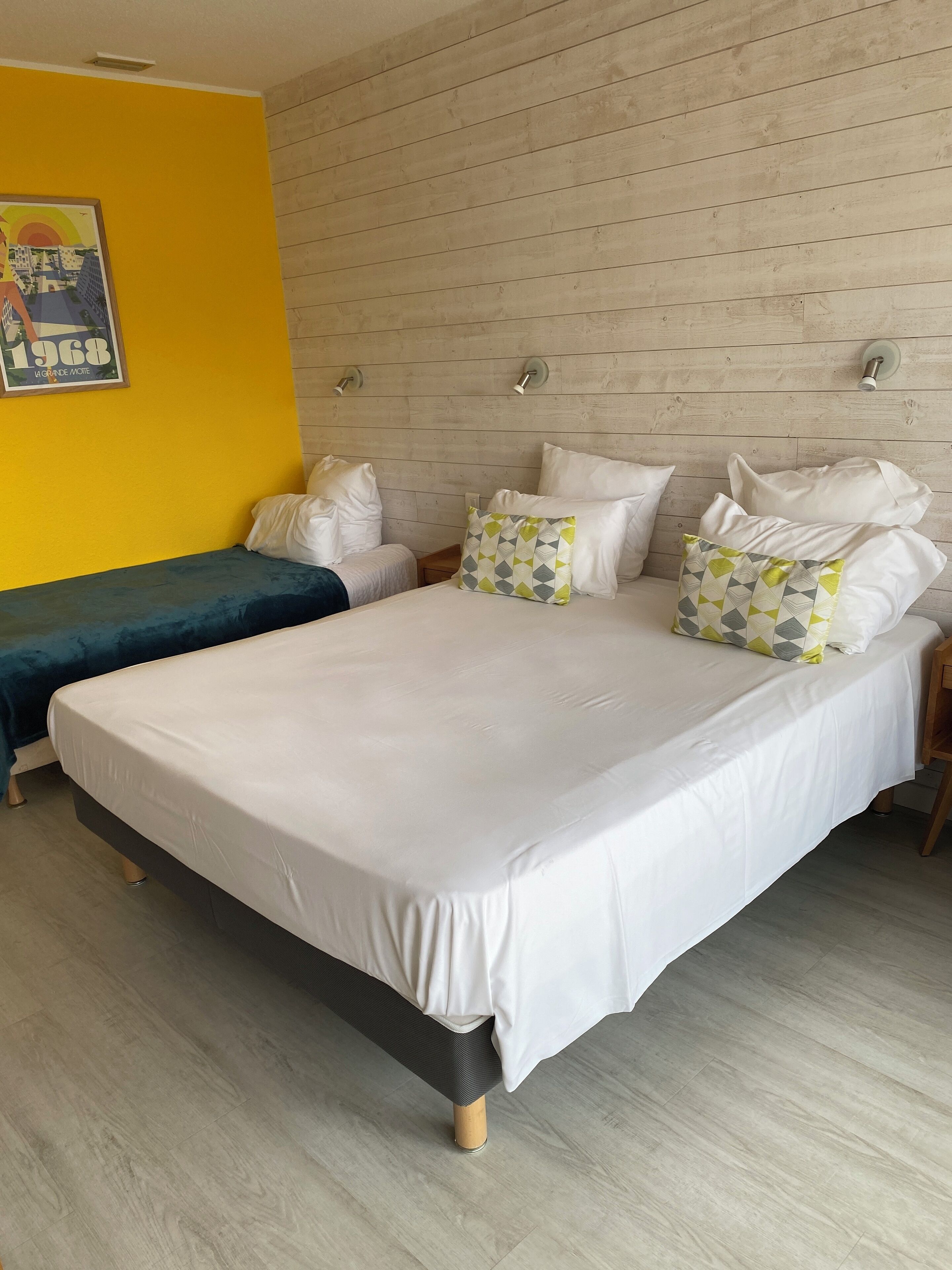 Un dormitorio con una cama grande, una cama más pequeña, paneles de madera en la pared y una pared de acento amarilla.