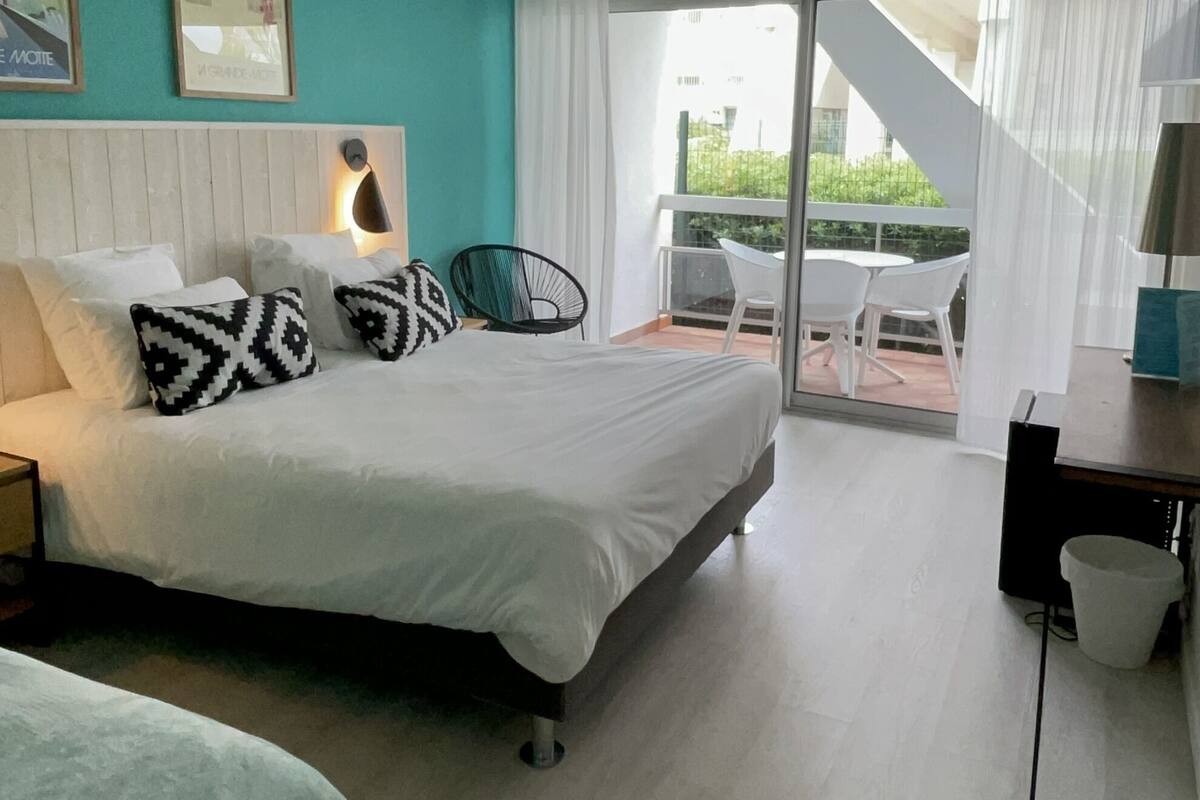 A modern hotel room with a large bed, a desk, and a balcony with outdoor seating.