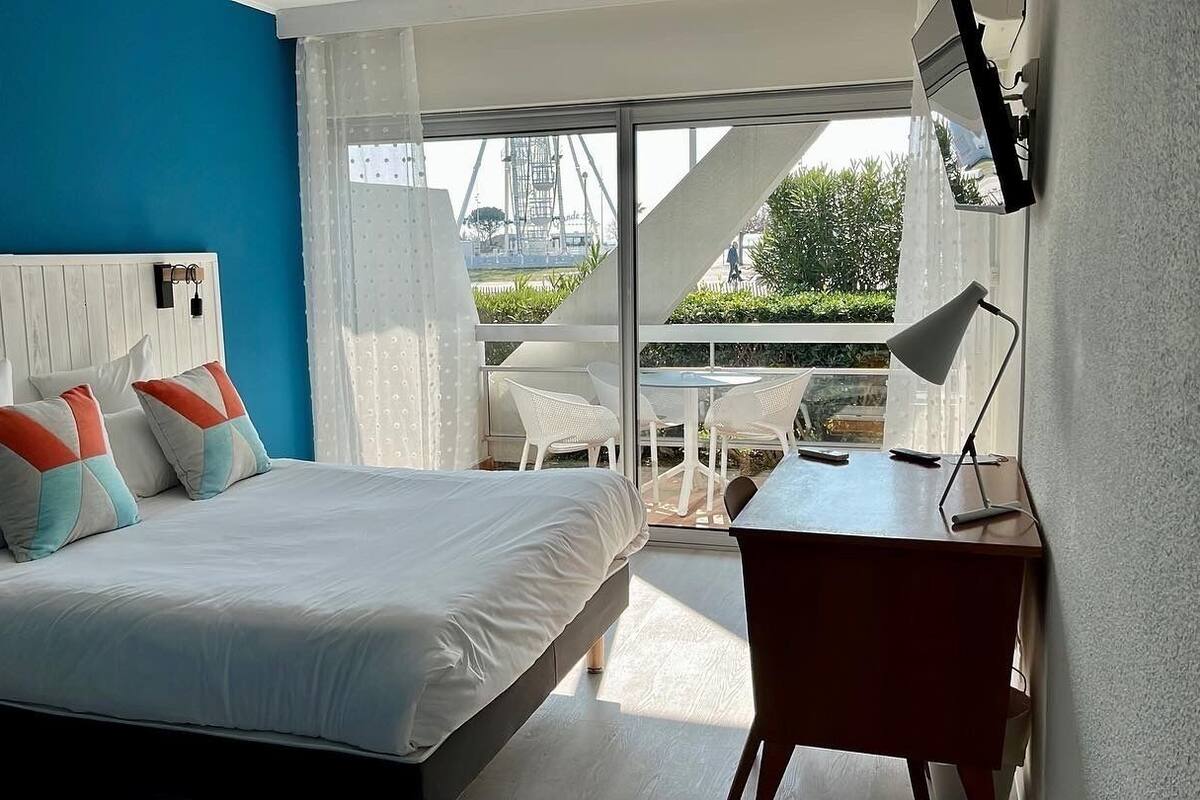 A modern hotel room with a large bed, a desk, and a balcony with a view of the city.