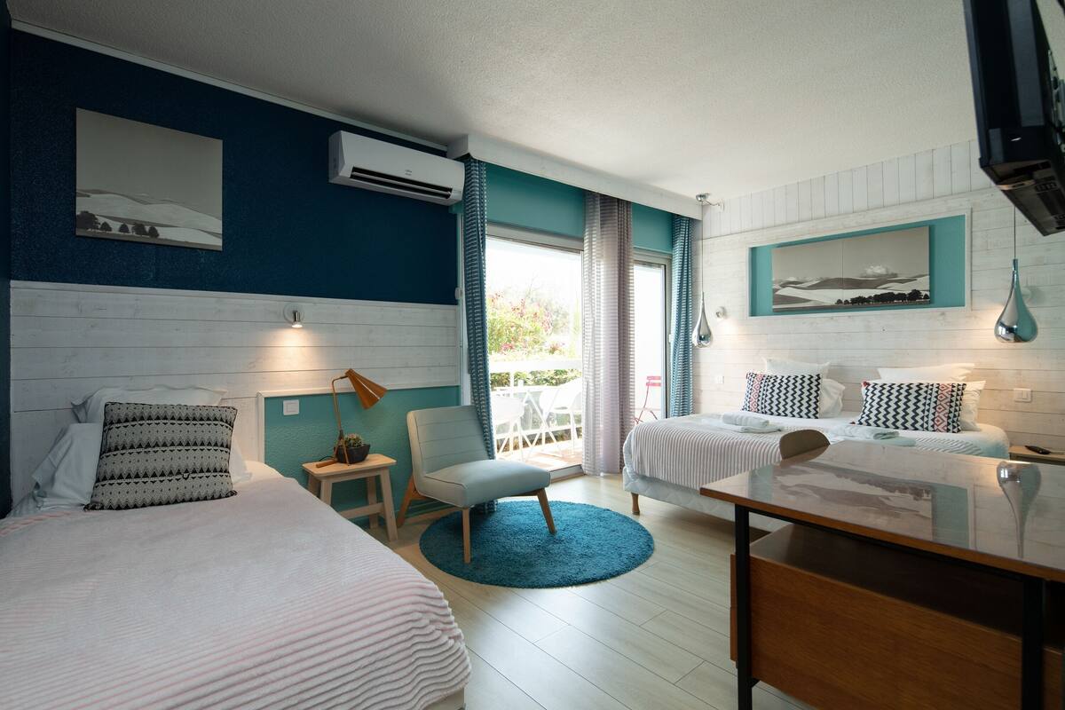 A hotel room with two beds, a desk, a chair, and a view of the outdoors.