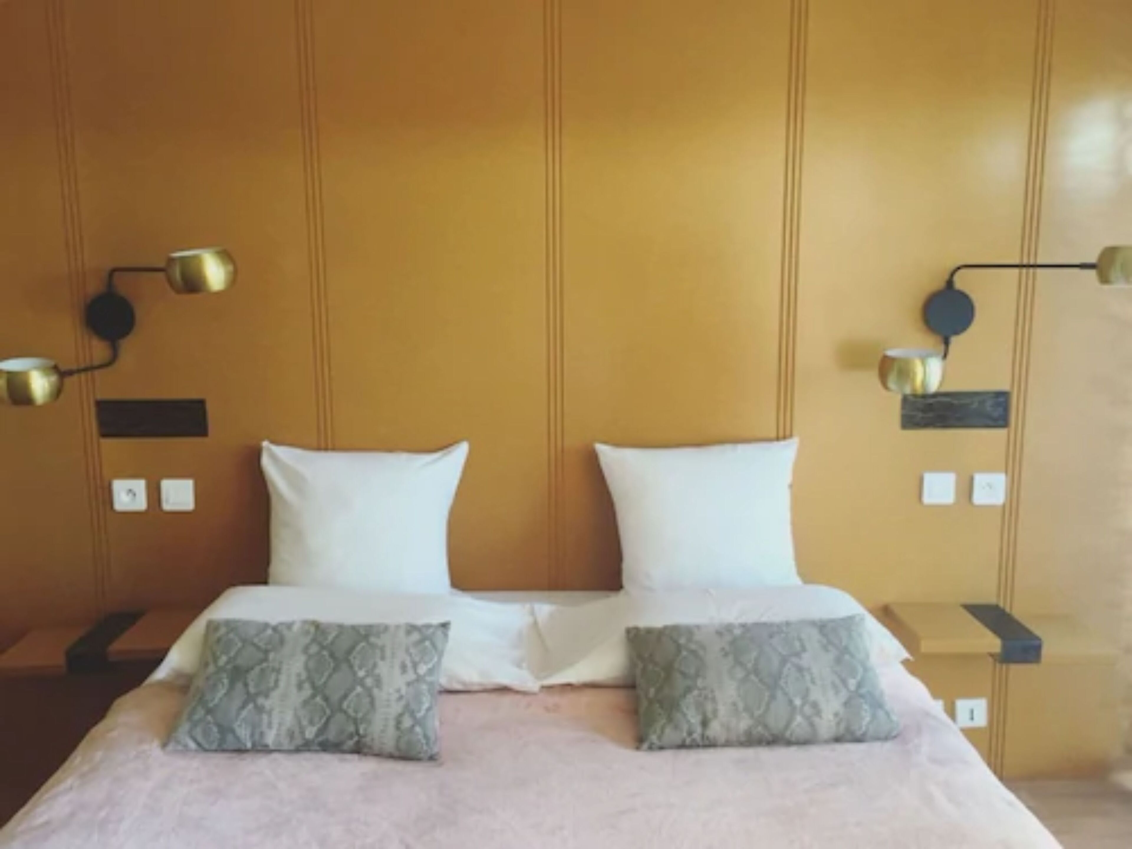 A double bed with two pillows, a bedside table with a lamp, and a wall-mounted light fixture.