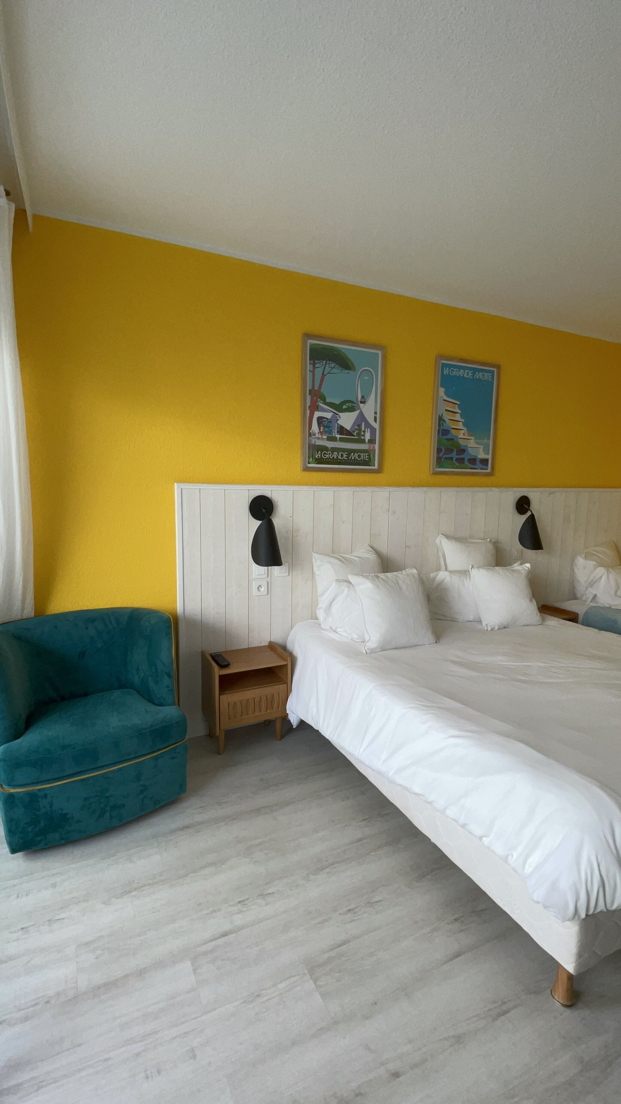 A bedroom with a bed, a nightstand, a teal armchair, and two wall art pieces.