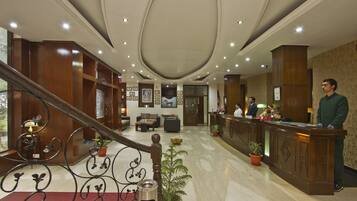 A hotel lobby with a reception desk, seating area, and a staircase.