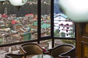 A room with a view of a town through large windows, featuring a table with a vase and two chairs.