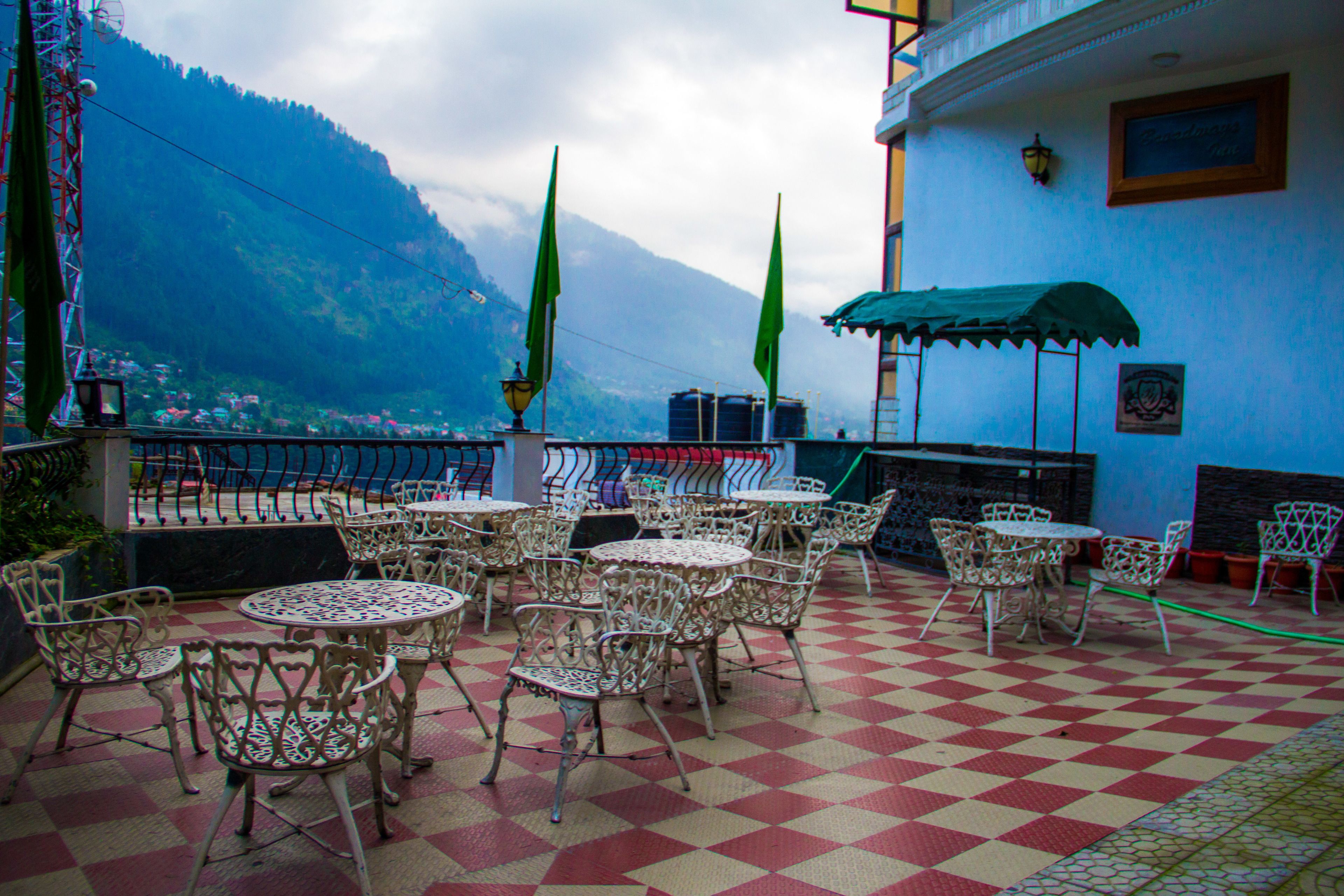 A terrace with outdoor seating, a checkered floor, and a mountainous backdrop.