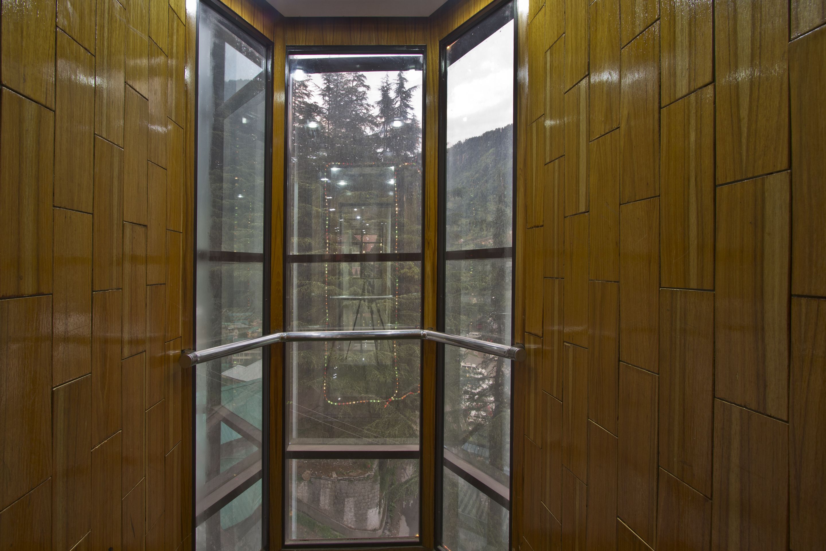 A corner of a room with wooden paneling and a large window with a metal railing.