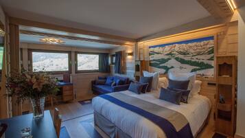 A bedroom with a large bed, a sofa, and a desk. There is a window with a view of mountains.