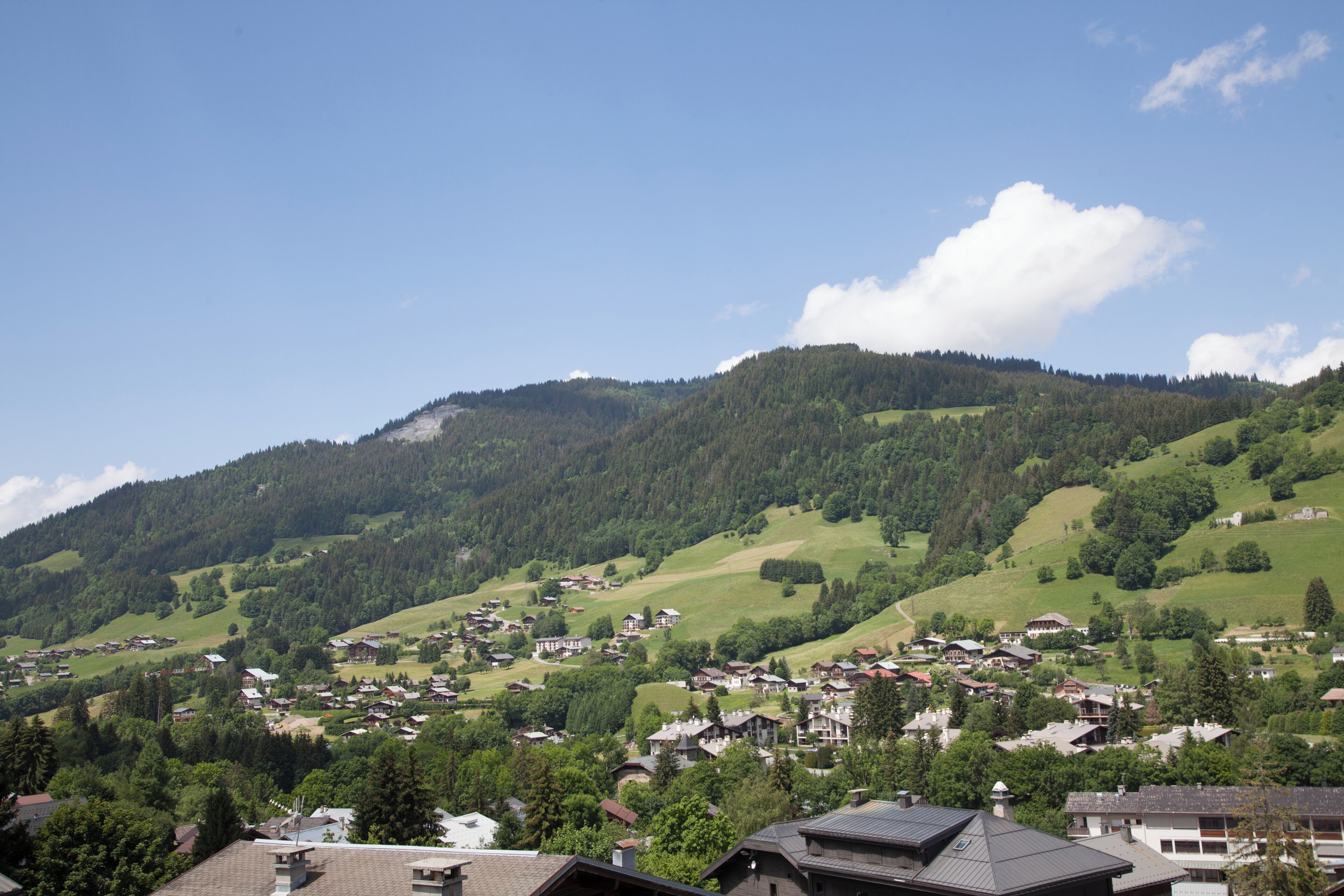 A village nestled in a valley with houses and buildings spread across the landscape, surrounded by green hills and a clear sky.